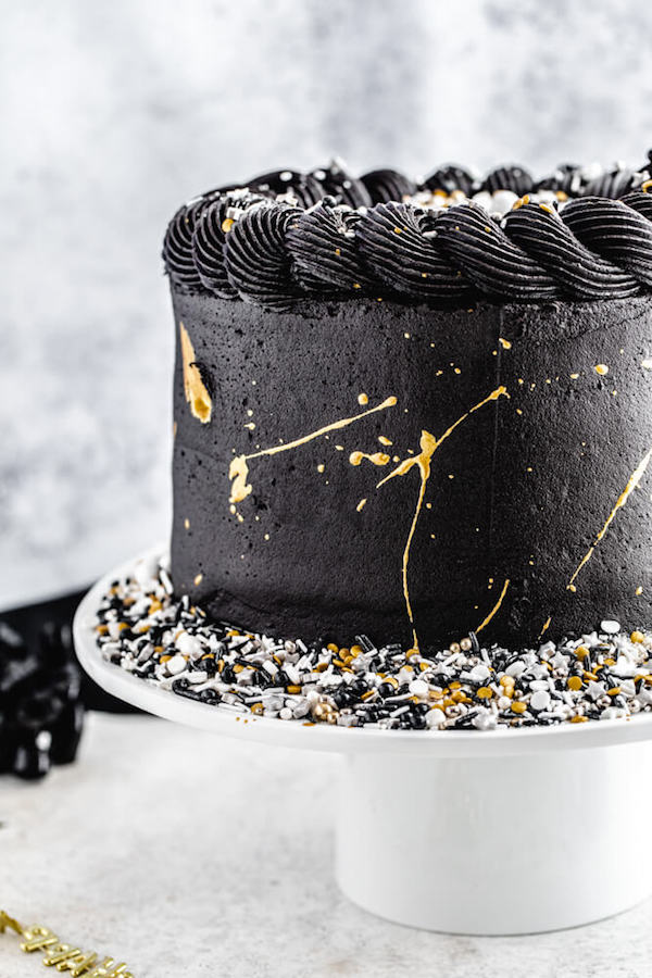 close up side view of black and gold cake with sprinkles on the cake stand