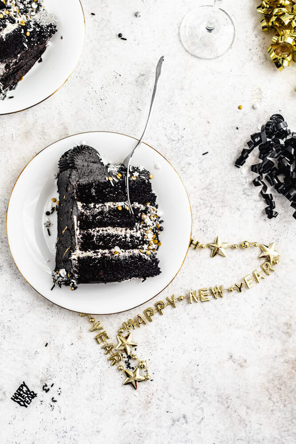 black cake on a white plate with fork inside and a happy new year's necklace underneath plate