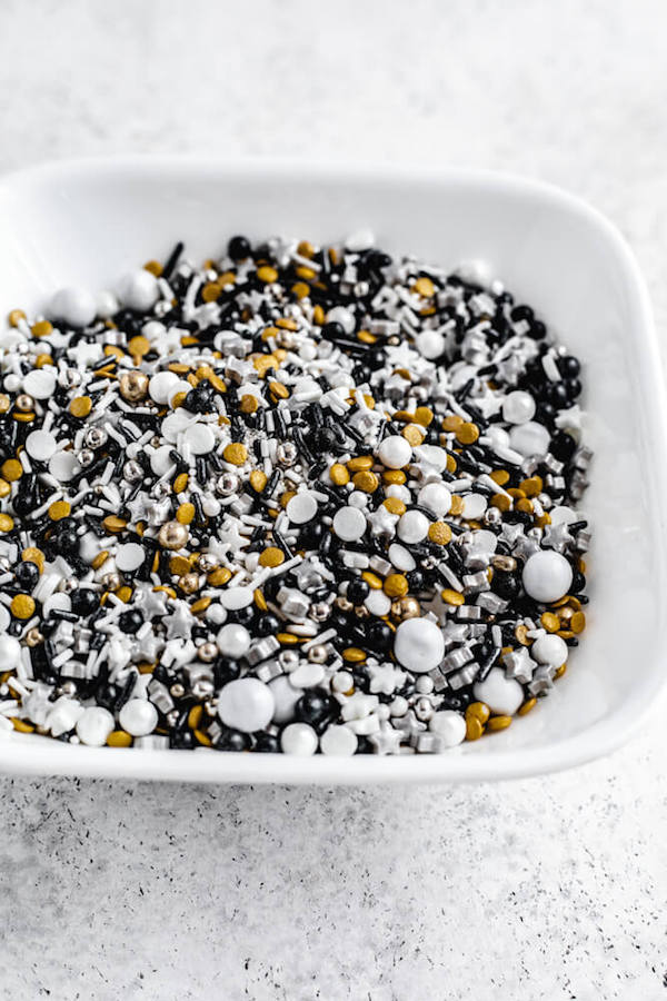 variety of black, gold, white and silver sprinkles in a white bowl