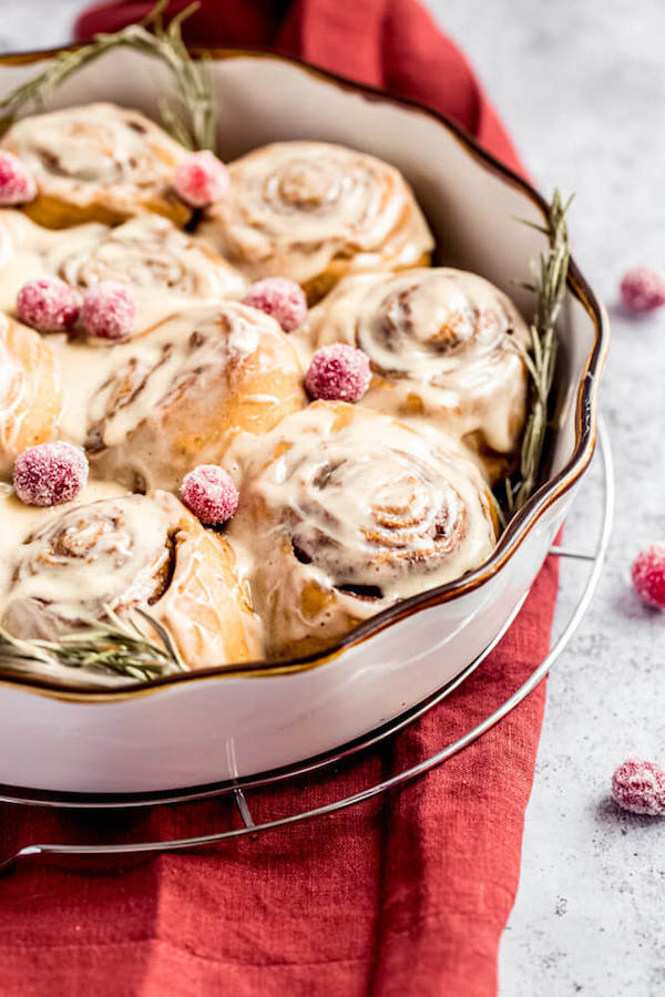 cinnamon rolls in a pie dish topped with sugared cranberries and rosemary 