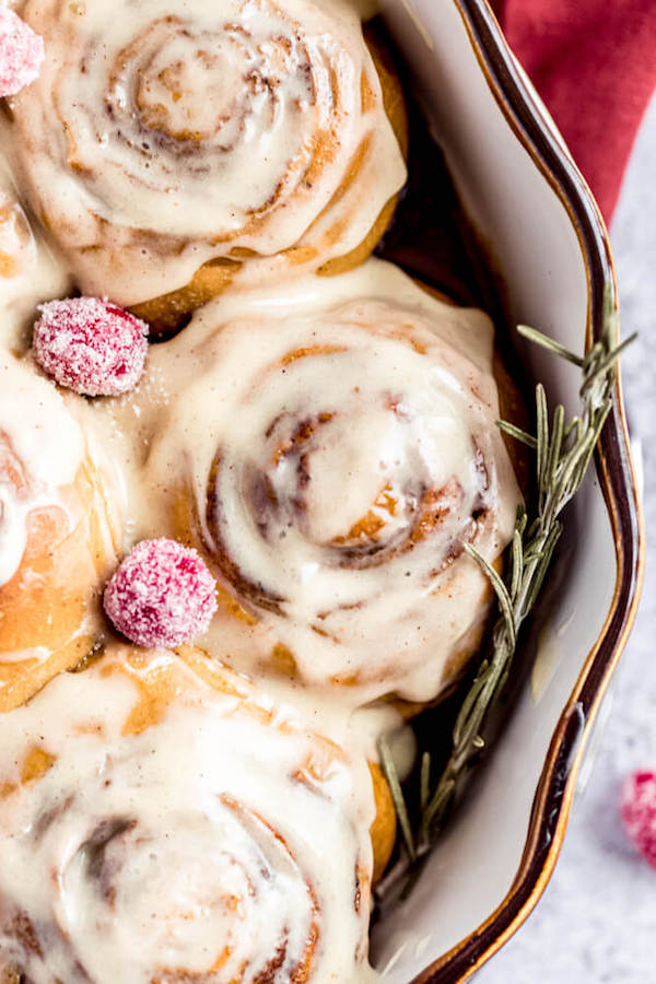 close up of cinnamon rolls topped with eggnog cream cheese icing and sugared cranberries