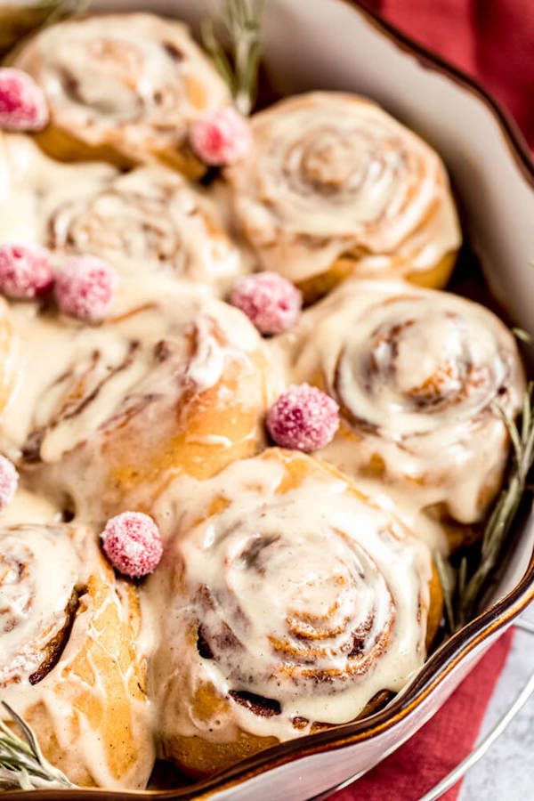 close up of cinnamon rolls topped with eggnog cream cheese icing and sugared cranberries