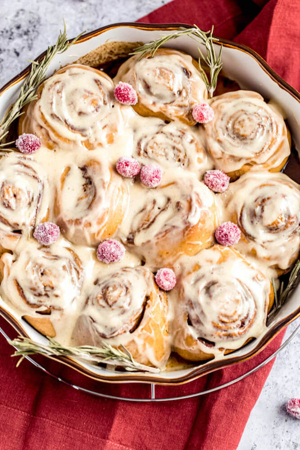 cinnamon rolls in a pie dish topped with sugared cranberries and rosemary 
