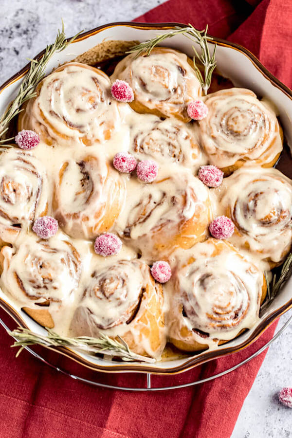 cinnamon rolls in a pie dish topped with sugared cranberries and rosemary 