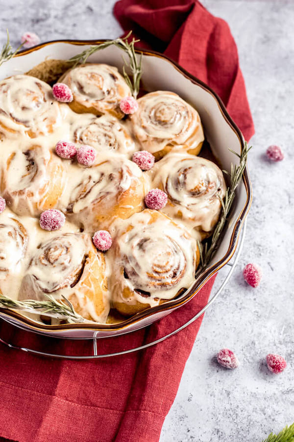 cinnamon rolls in a pie dish topped with sugared cranberries and rosemary 