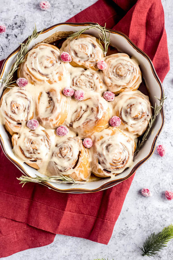 cinnamon rolls in a pie dish topped with sugared cranberries and rosemary 