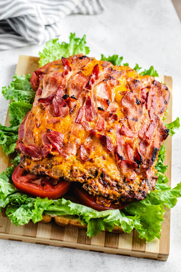 bacon and cheese topped rectangle burger patty on a lettuce and tomato covered slider bun