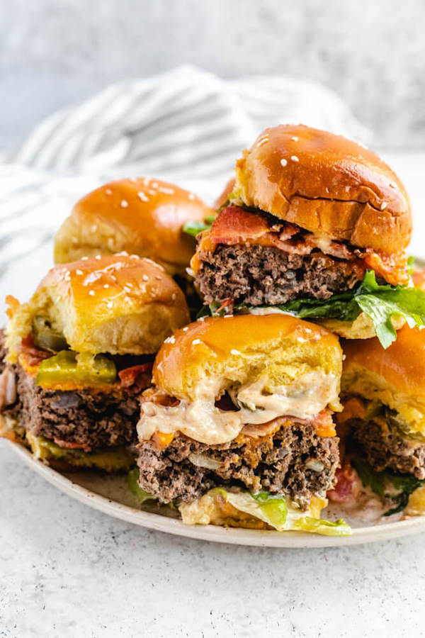 small bacon cheeseburgers piled onto a white plate