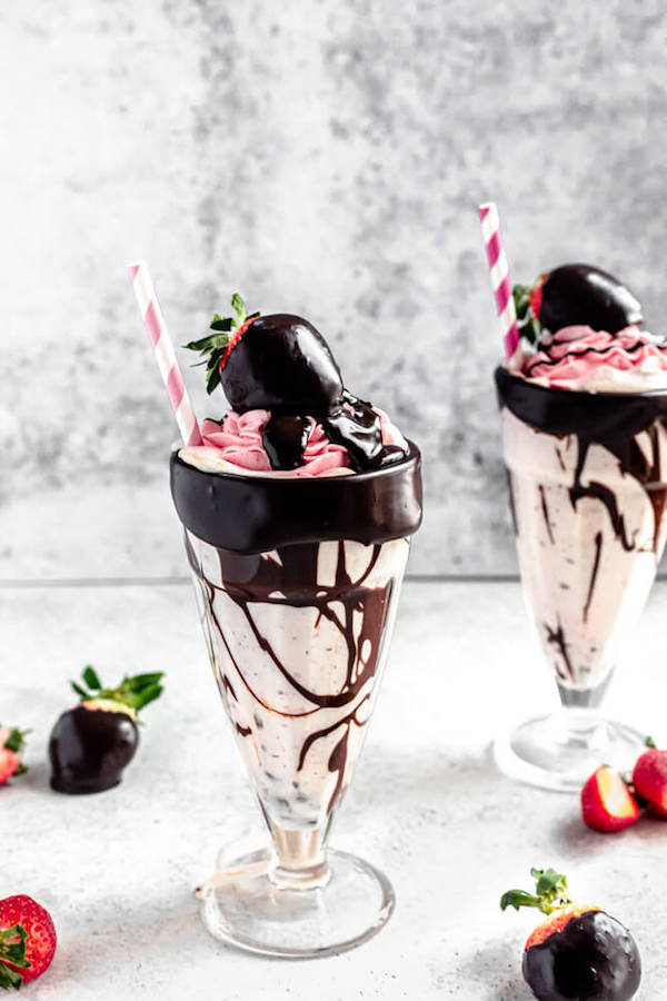 two glasses of milkshakes topped with ganache dipped strawberries