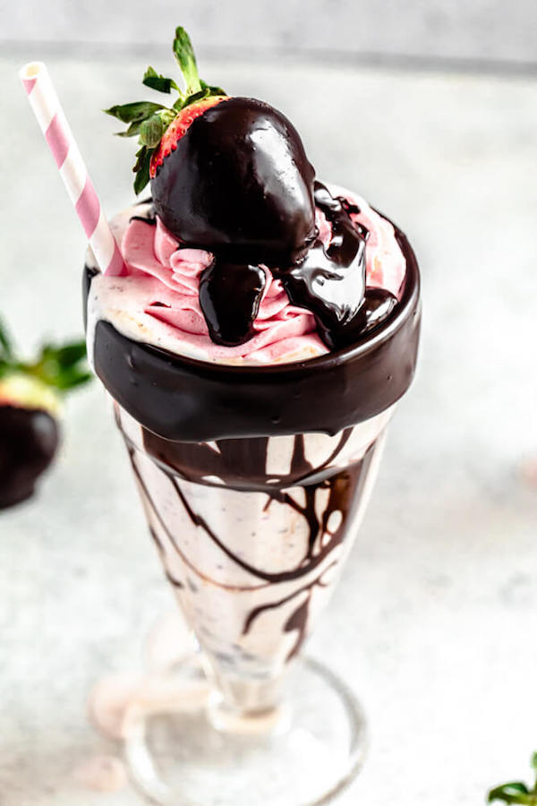 close up of strawberry and chocolate chip milkshake topped with strawberry whipped cream and a ganache coated strawberry