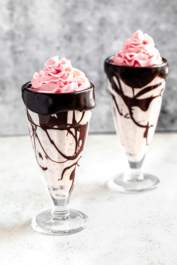 two glasses of strawberry whipped cream topped milkshakes