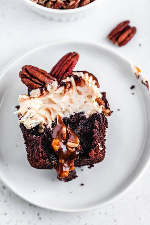 chocolate cupcake cut in half with caramel pecan filling inside on a white plate