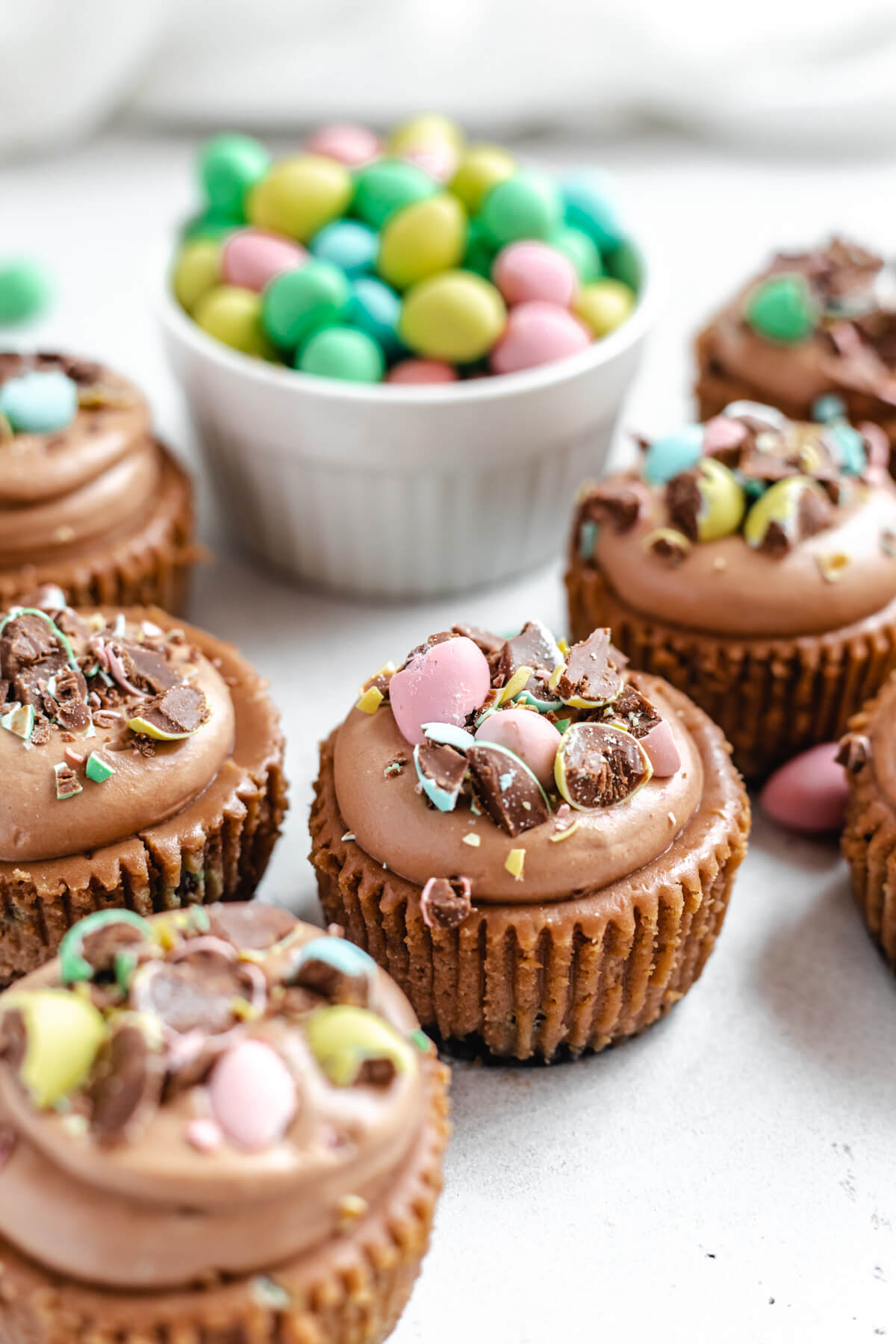 close up of multiple cheesecake cupcakes topped with mousse and chopped mini eggs