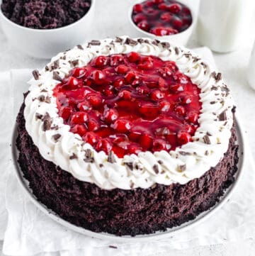 Black Forest cheesecake on a white plate with cake crumbs and cherry pie filling in white bowls