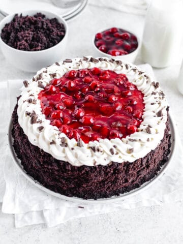 Black Forest cheesecake on a white plate with cake crumbs and cherry pie filling in white bowls