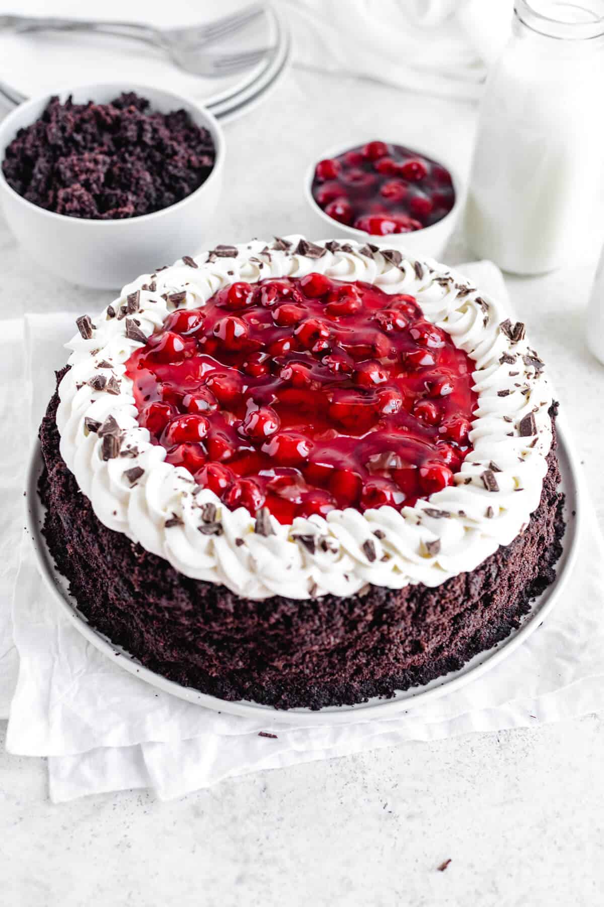 Black Forest cheesecake on a white plate with cake crumbs and cherry pie filling in white bowls