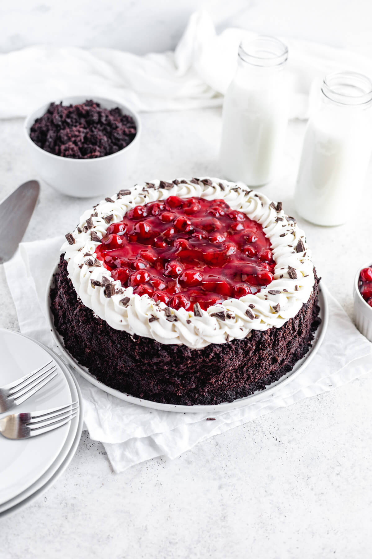 cake covered cheesecake on a white platter with milk bottles, stack of plates and cake crumbs around it