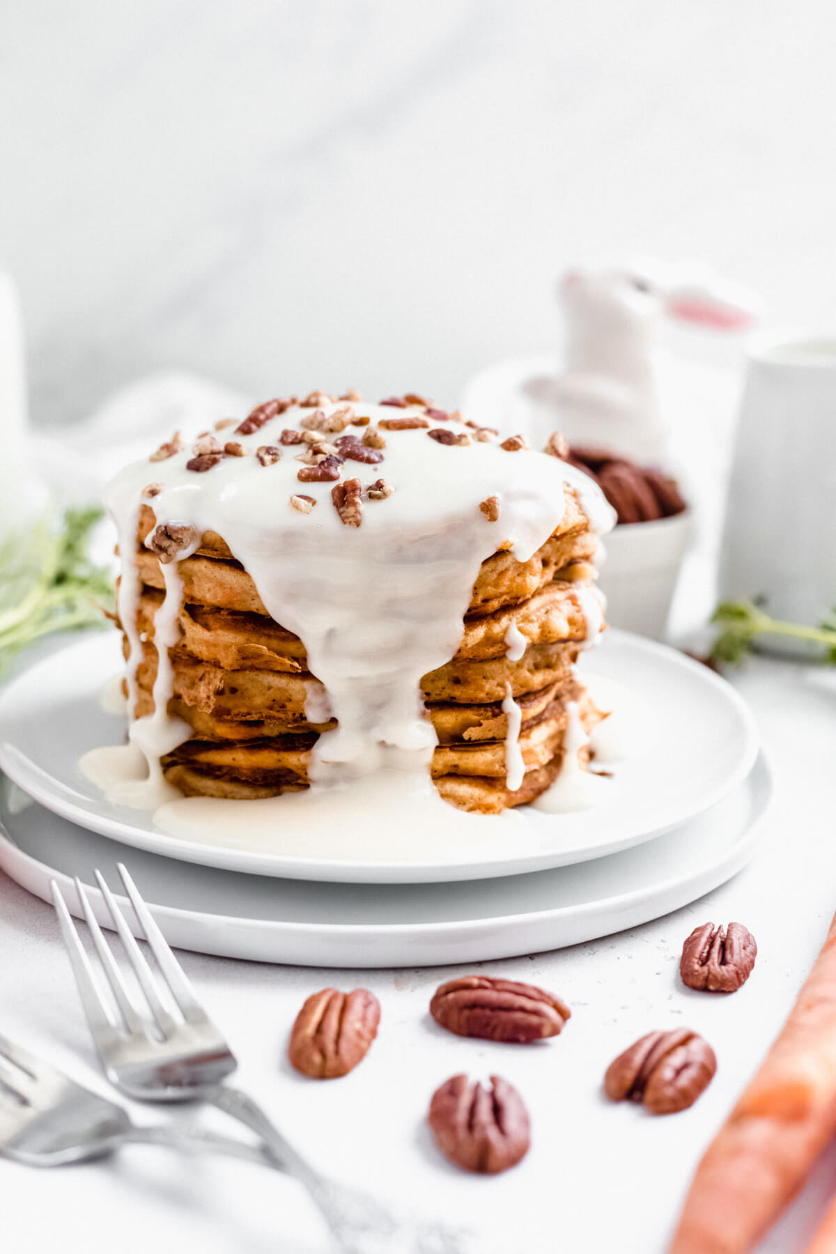 stack of pancakes on two white plates with two forks and pecans in front