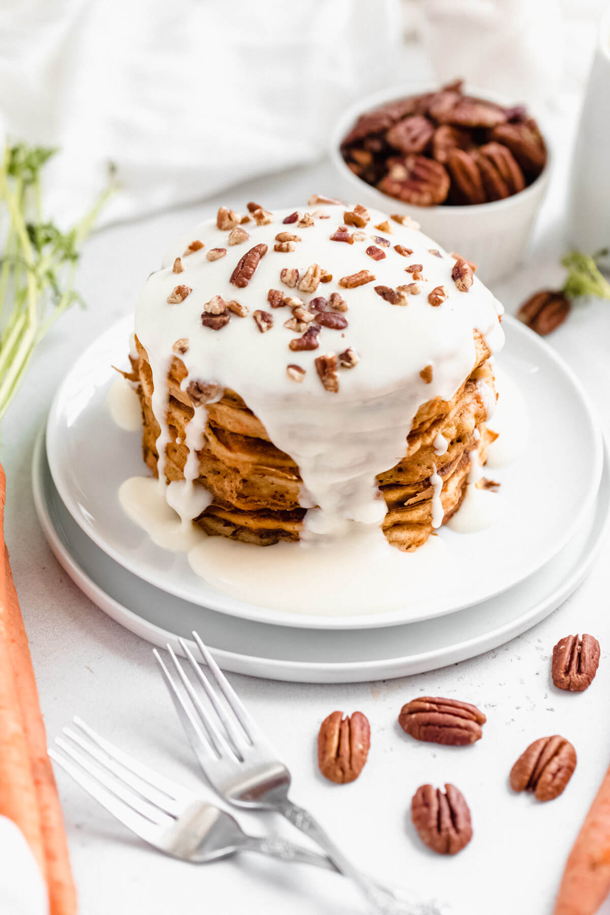 stack of pancakes topped with cream cheese glaze and chopped pecans