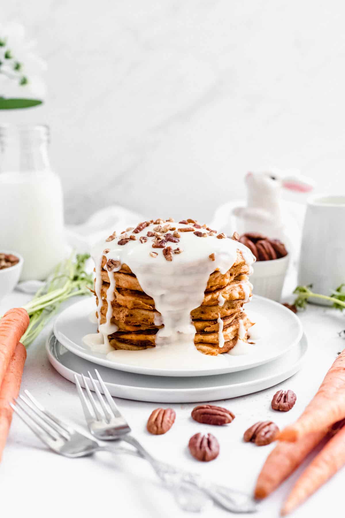 pancake stack on two white plates with two forks, carrots and pecans around it