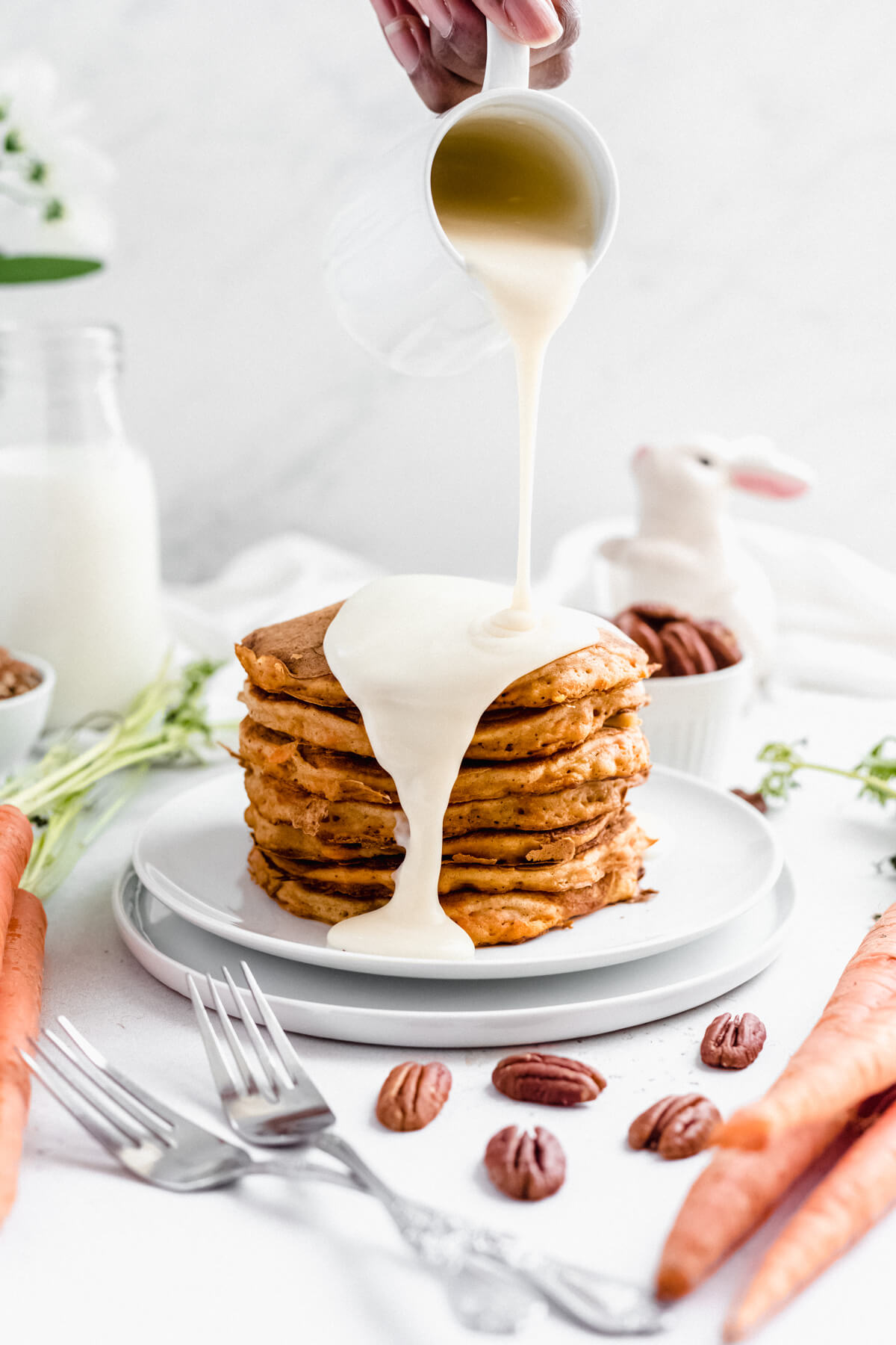 pouring cream cheese glaze onto a stack of pancakes