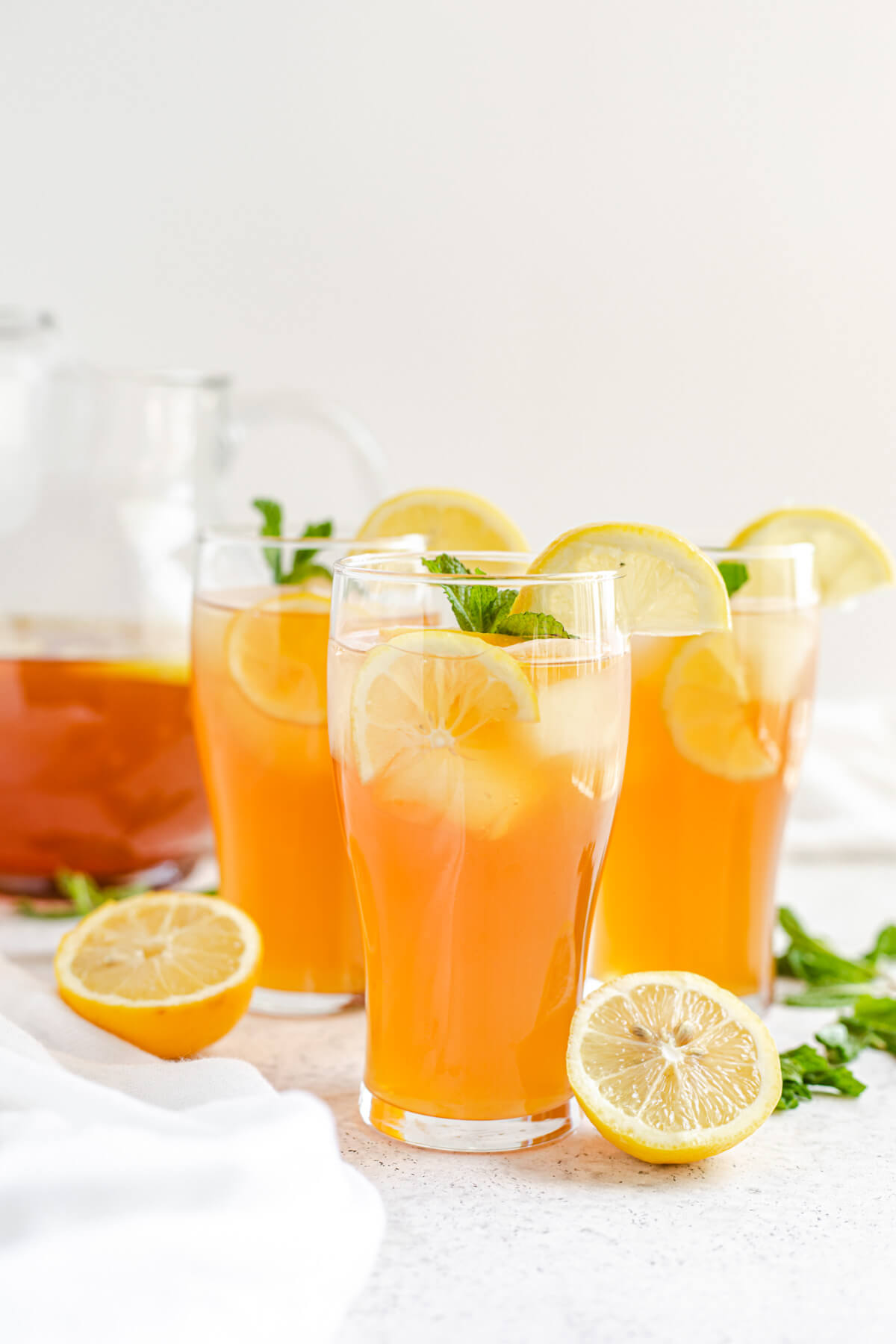 three glasses of iced tea with a glass pitcher in the background