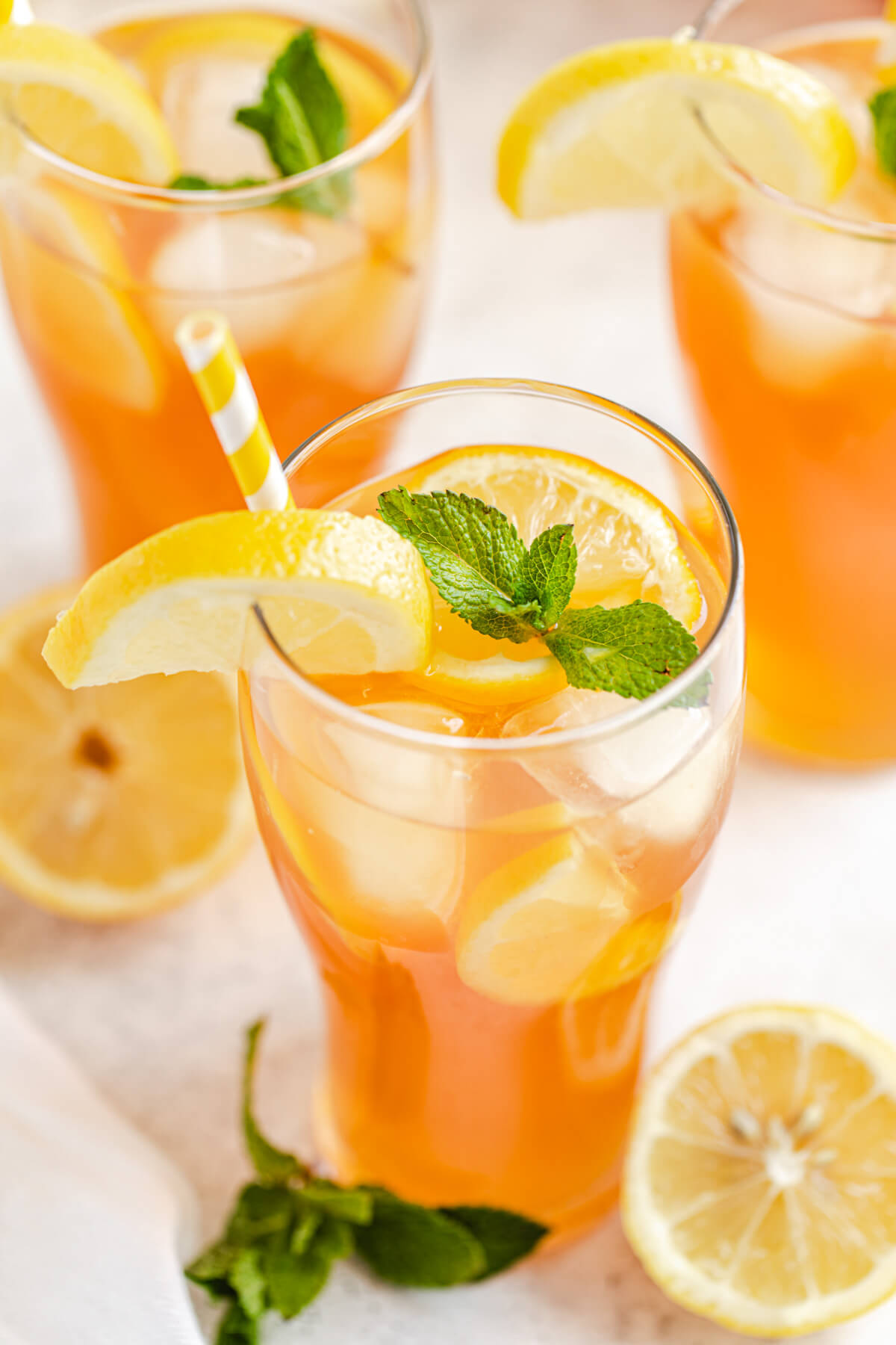 close up showing the inside of a glass filled with iced tea, ice cubes, mint leaves, lemon slices and a yellow straw