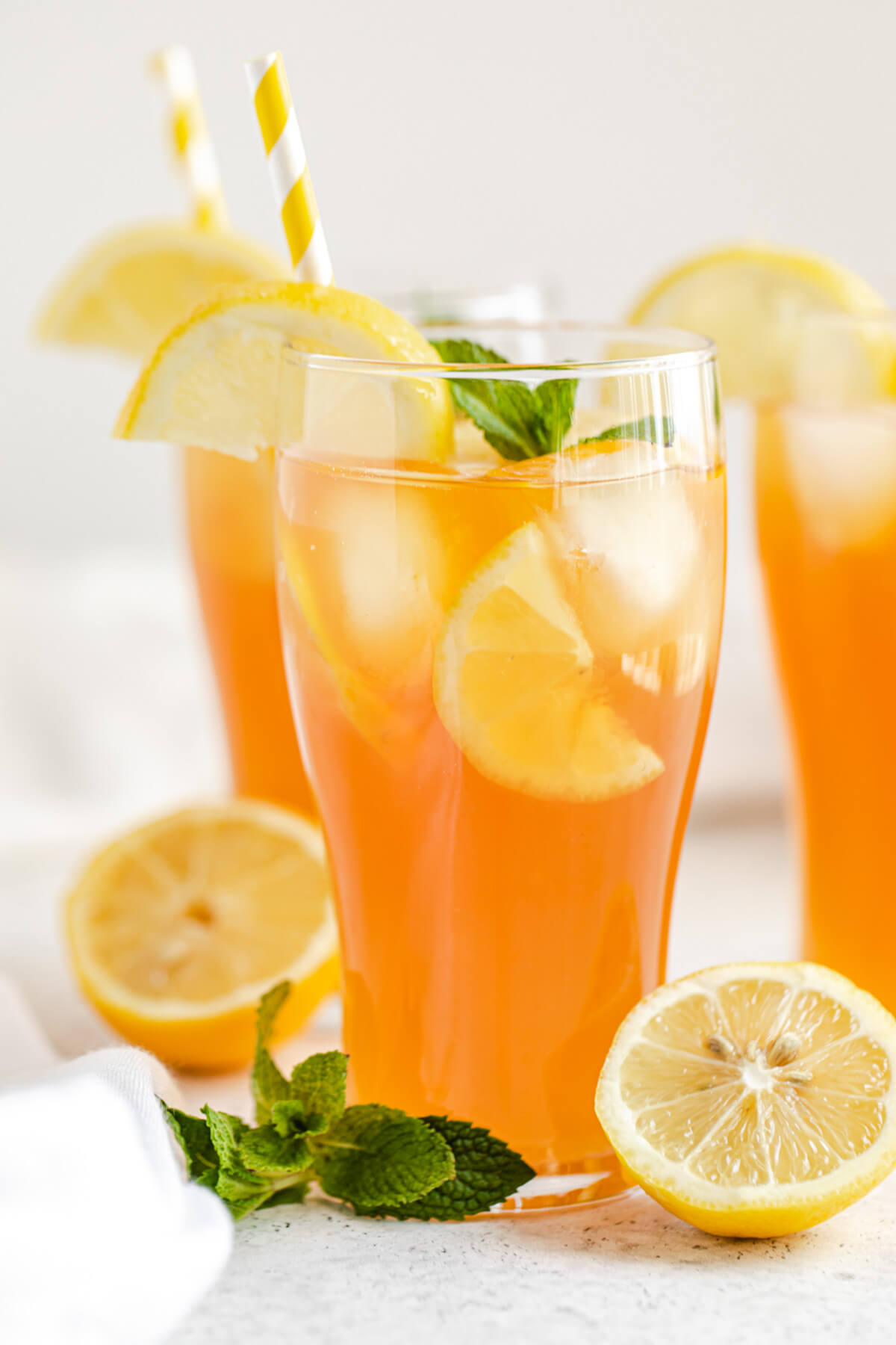 close up of three glasses of sweet tea with halved lemons and mint leaves inside and around the glasses