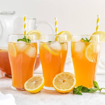 three glasses of iced tea with yellow striped straws and lemons and mint leaves in front of glasses