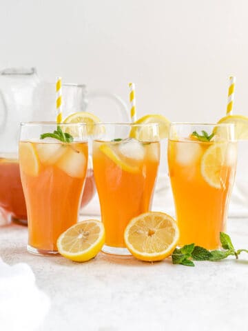 three glasses of iced tea with yellow striped straws and lemons and mint leaves in front of glasses