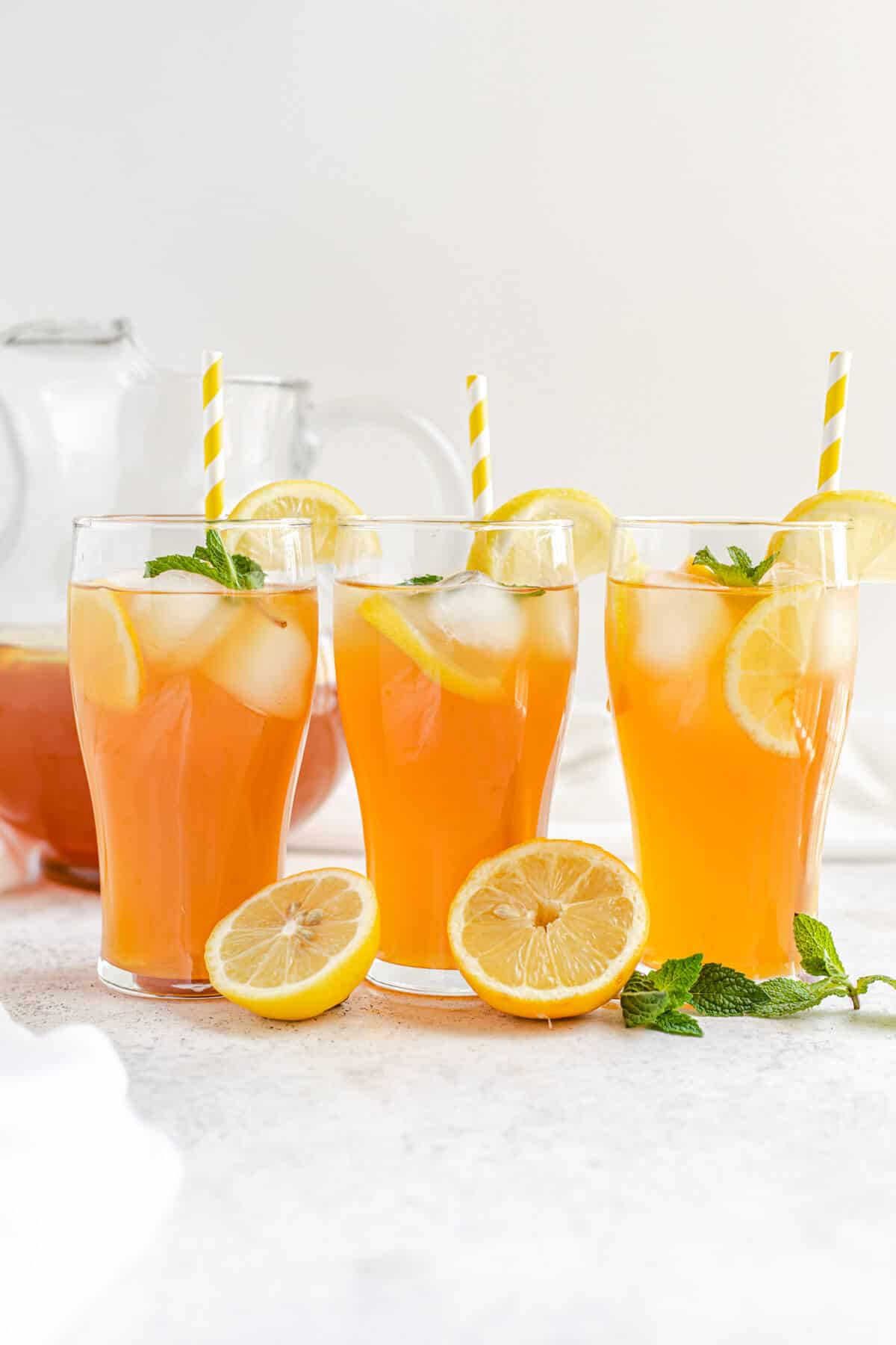 three glasses of iced tea with yellow striped straws and lemons and mint leaves in front of glasses