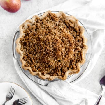 top of crumble pie with two apples, white scarf and white plates