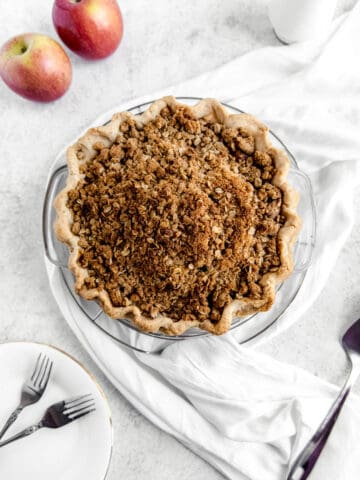 top of crumble pie with two apples, white scarf and white plates