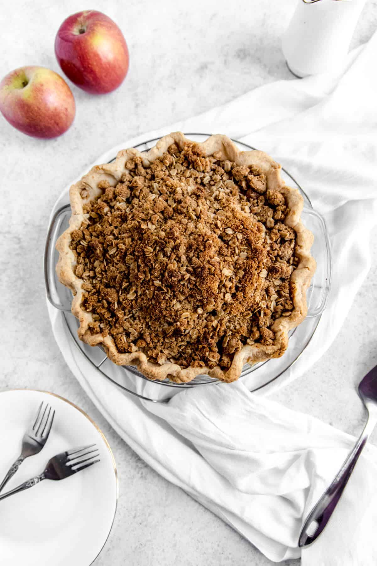 top of crumble pie with two apples, white scarf and white plates