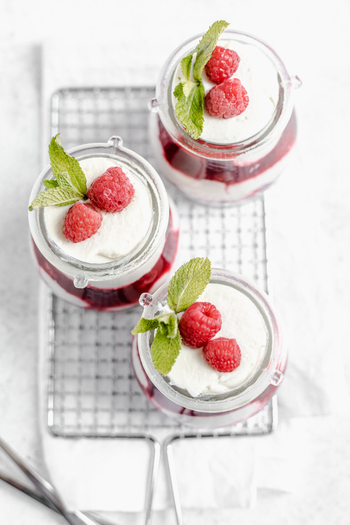 top view of three mousse jars topped with raspberries and mint leaves on a safety grater