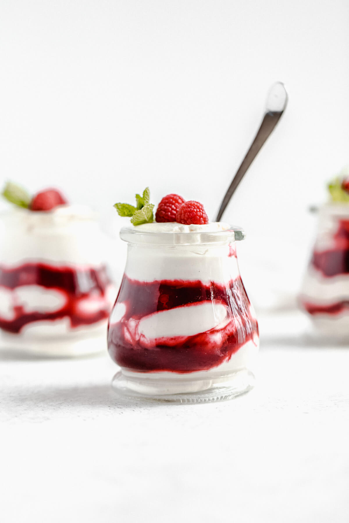 three jars of mousse with raspberry sauce and a spoon inside the one in the front