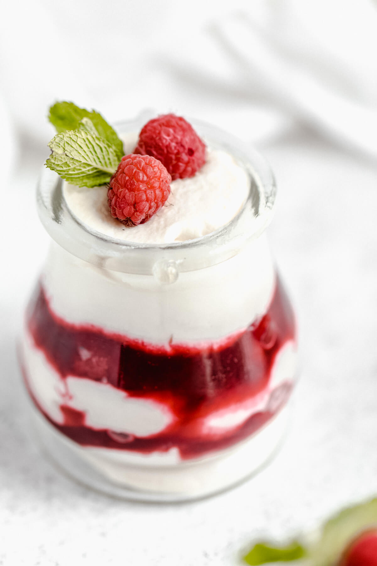 close up of raspberry mousse cups topped with fresh raspberries and mint leaves