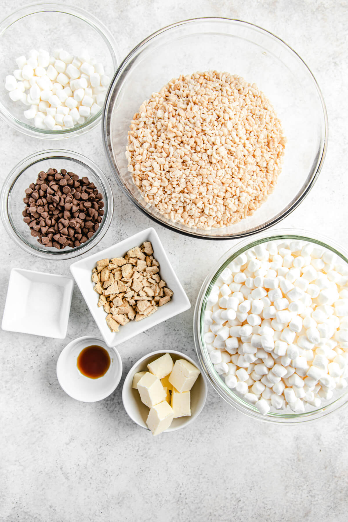 ingredient photo: bowls of Rice Krispies cereal, mini marshmallows, cubed butter, vanilla, salt, milk chocolate chips and crushed graham crackers