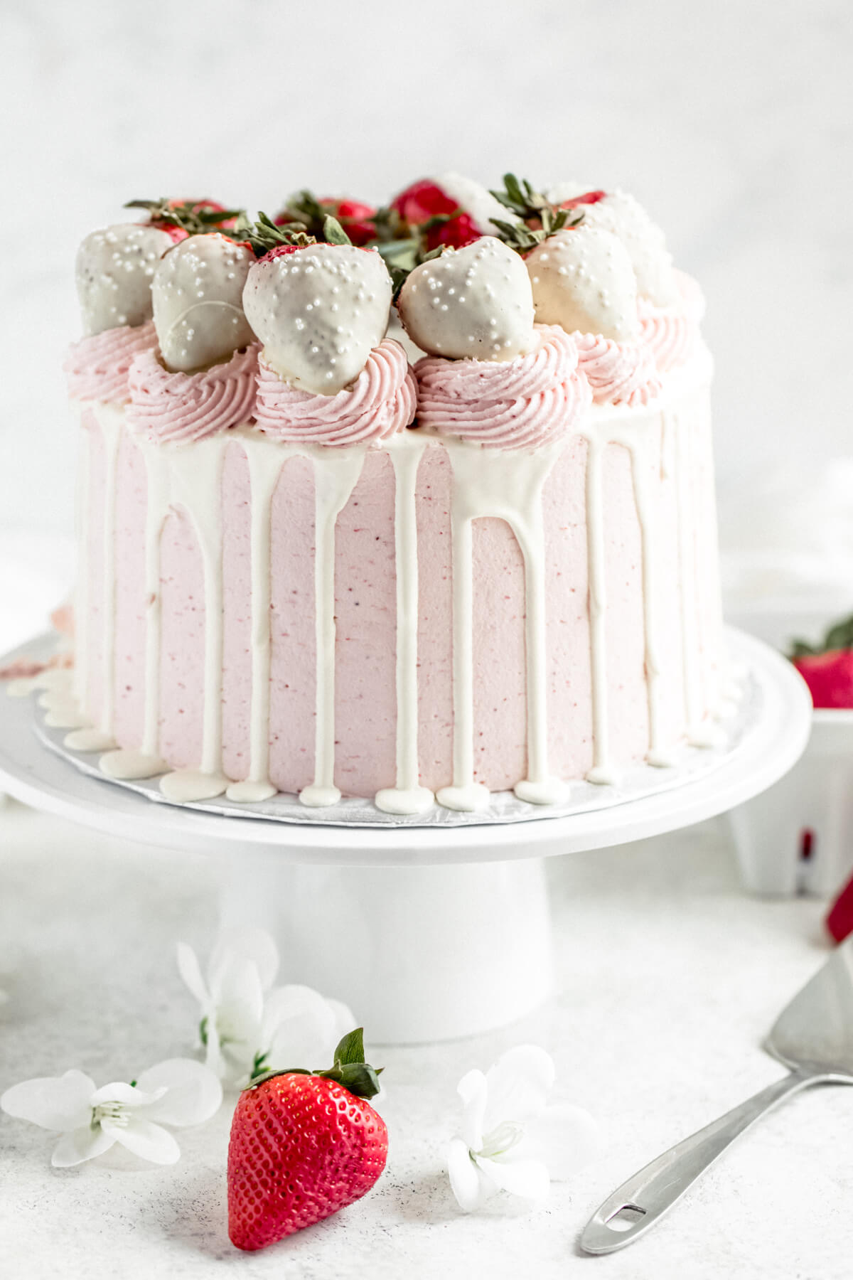 strawberry and white chocolate cake on a cake stand with strawberries in the background