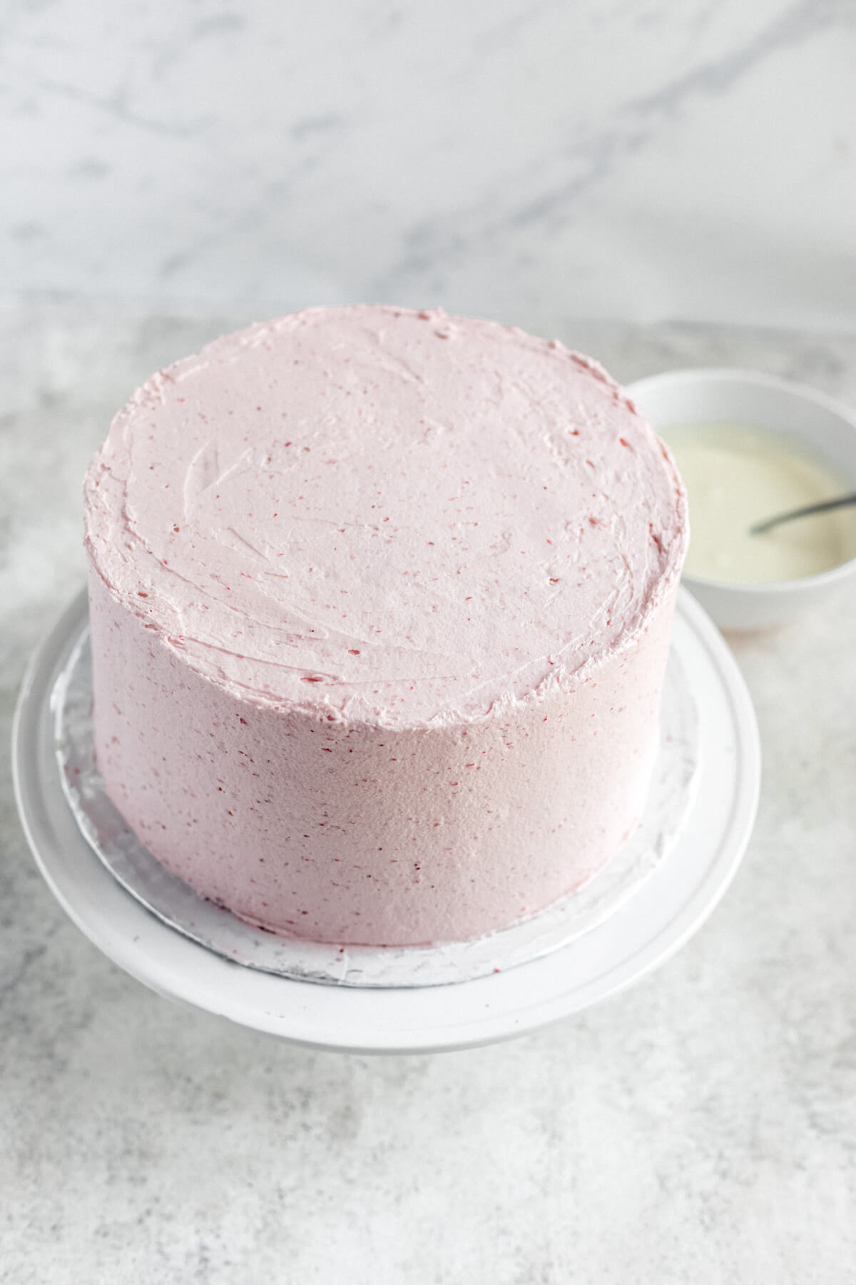 frosted cake on a cake stand with white chocolate ganache in the background