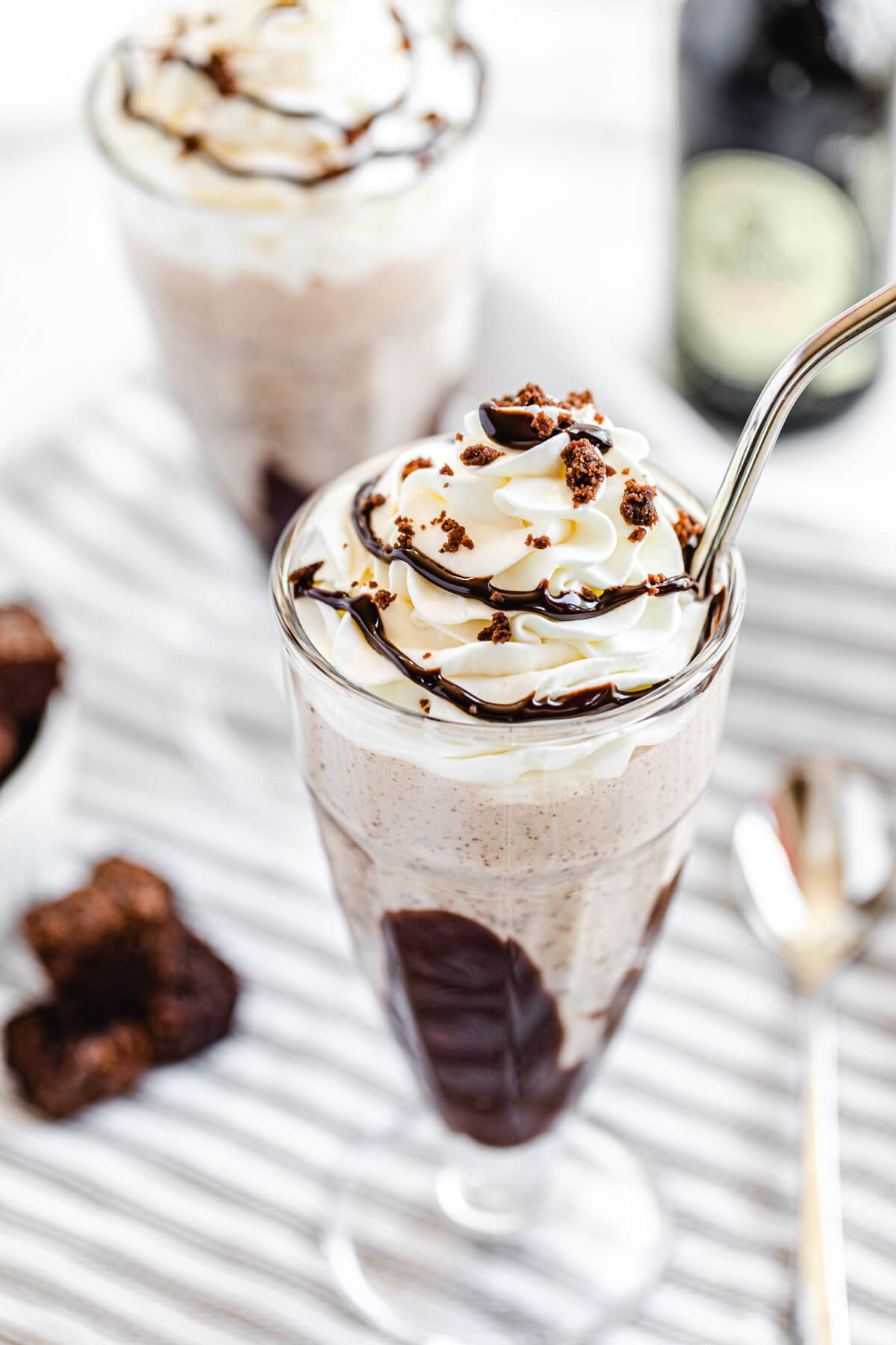 angled view of two milkshakes, brownies and spoon on a striped dish towel