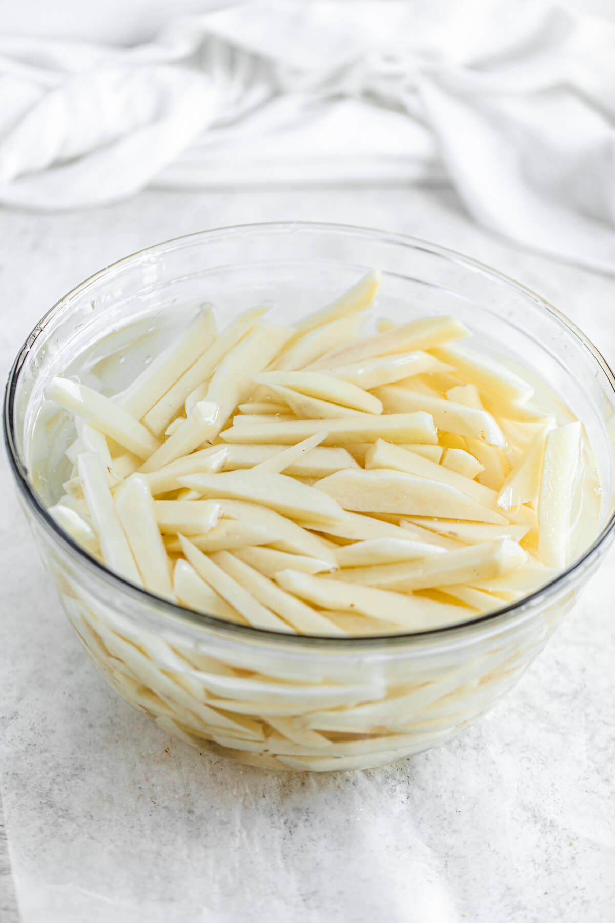 potato French fry sticks in a large glass bowl of cold water