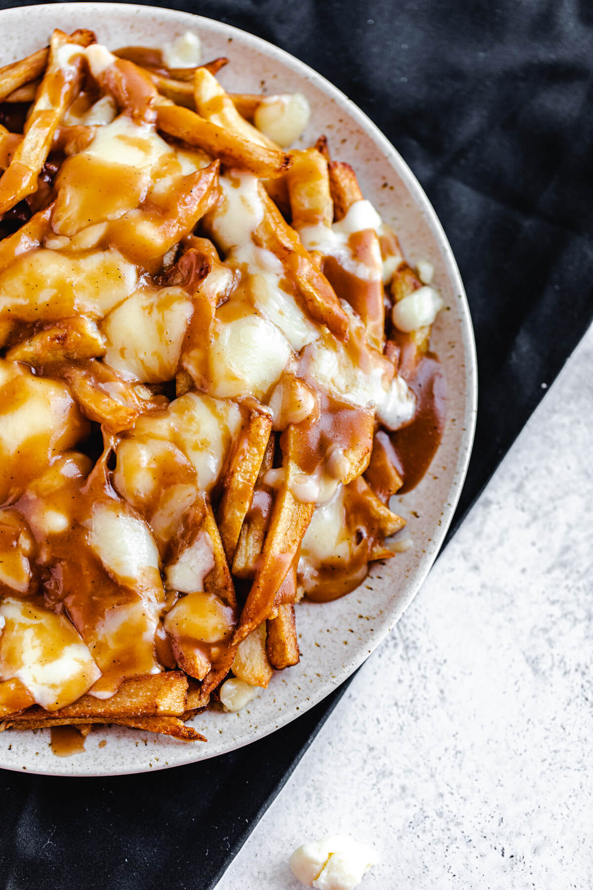 plate of fries, melted cheese and gravy on a black napkin