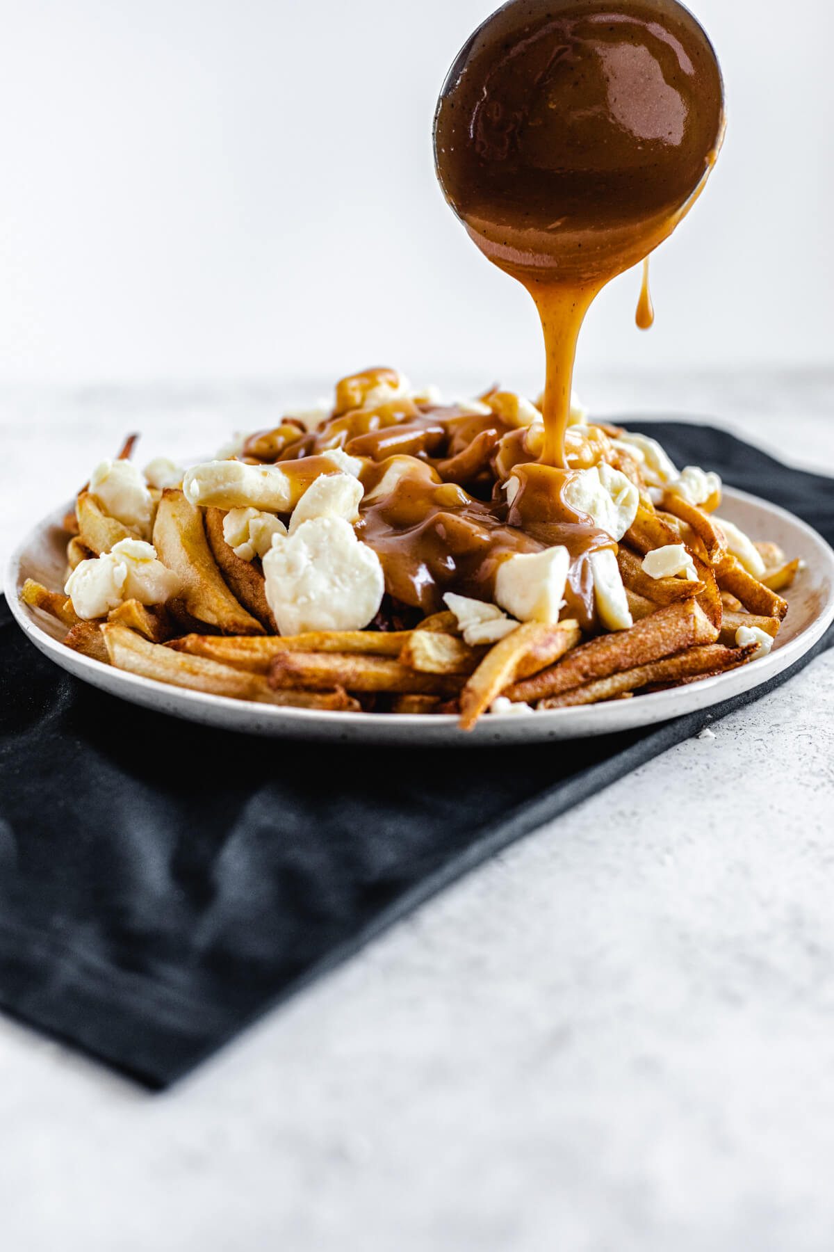 pouring gravy from a ladle onto a plate of fries and cheese curds