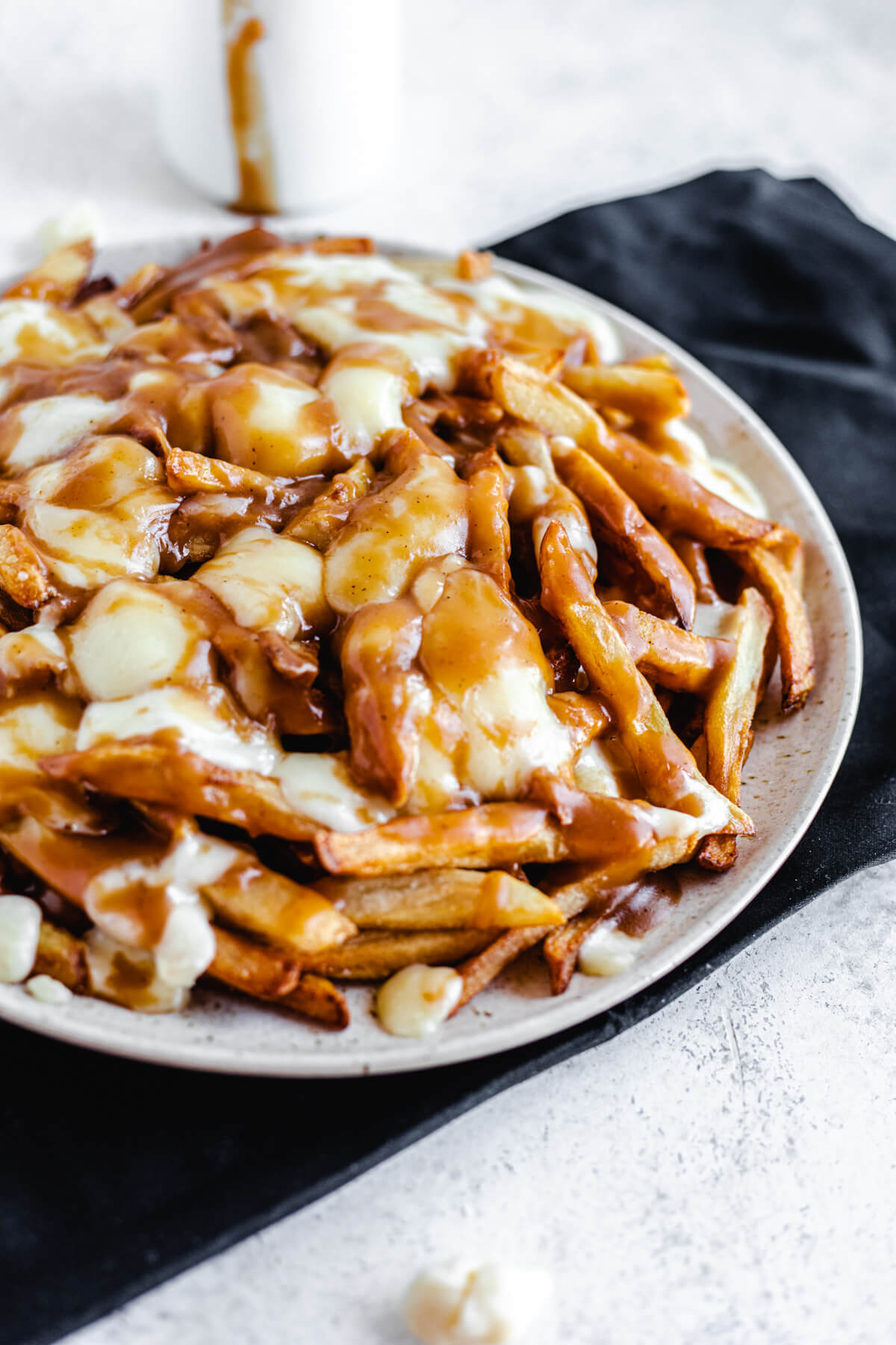 plate filled with homemade fries, cheese curds and brown gravy on a black rectangle cloth napkin