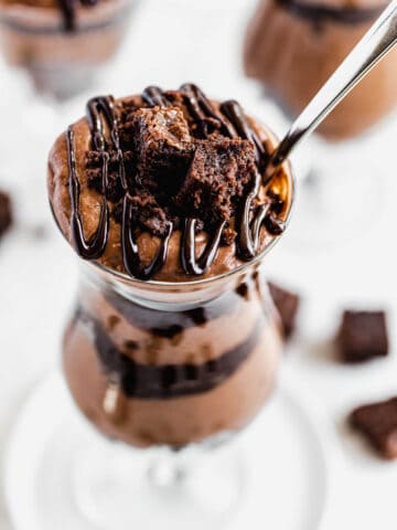 close up of chocolate mousse and brownies in a tall glass with a spoon