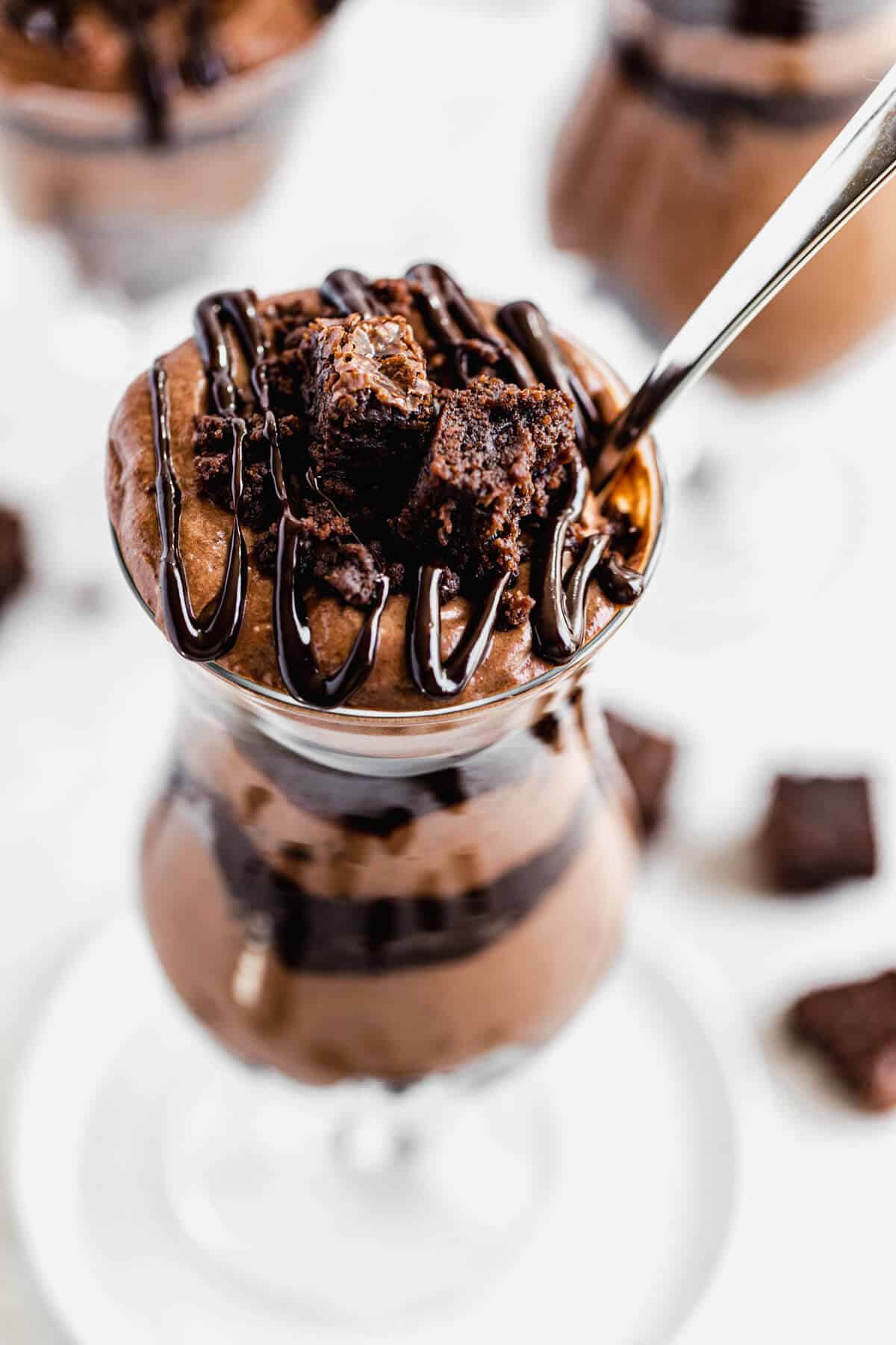 close up of chocolate mousse and brownies in a tall glass with a spoon
