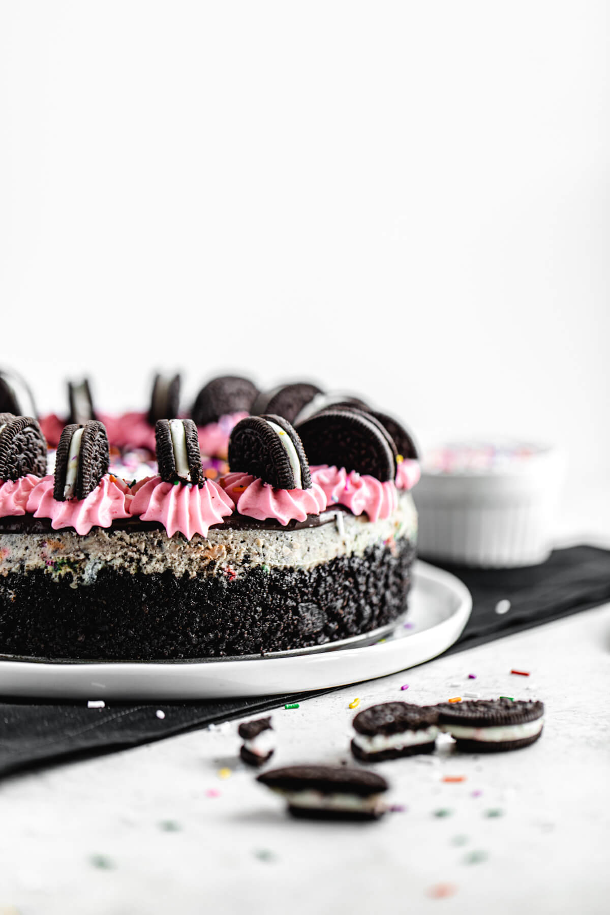 side view of cheesecake on a white platter with chopped Oreos in front of it