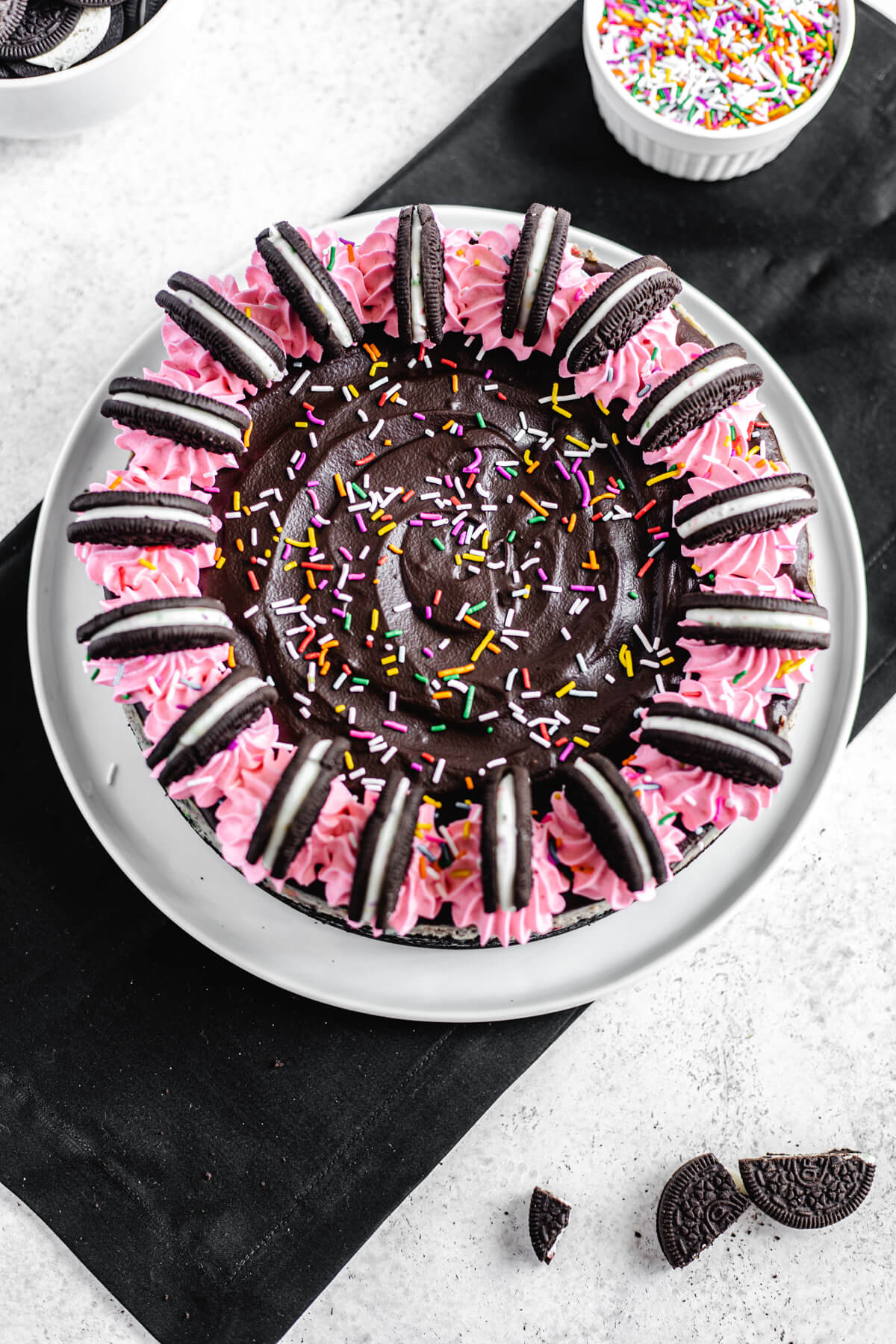 top view of cheesecake topped with pink whipped cream, rainbow sprinkles and halved Oreos