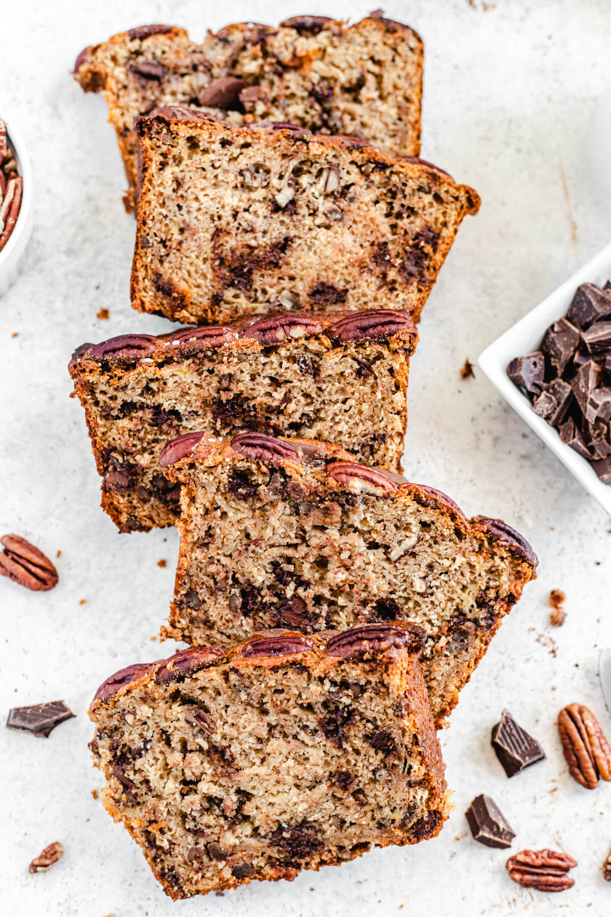 top shot of a row of banana bread slices with pecans and chocolate around them